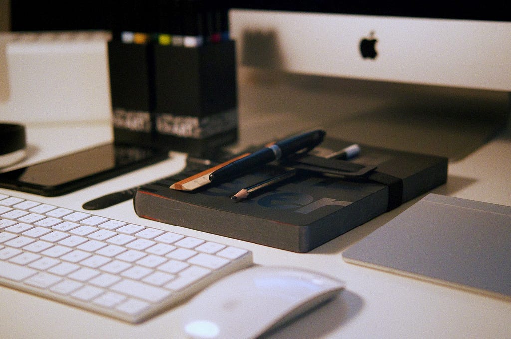 Keyboard, computer mouse, and various stationary neatly organized below a computer screen.