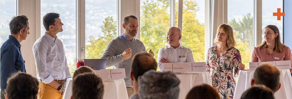 A panel discussion in front of windows showing trees in fall colors