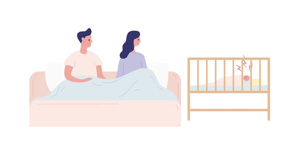 A couple sits in bed looking over at their sleepless baby in a crib.