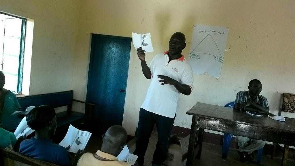 A man stands in a classroom holding up a piece of paper.