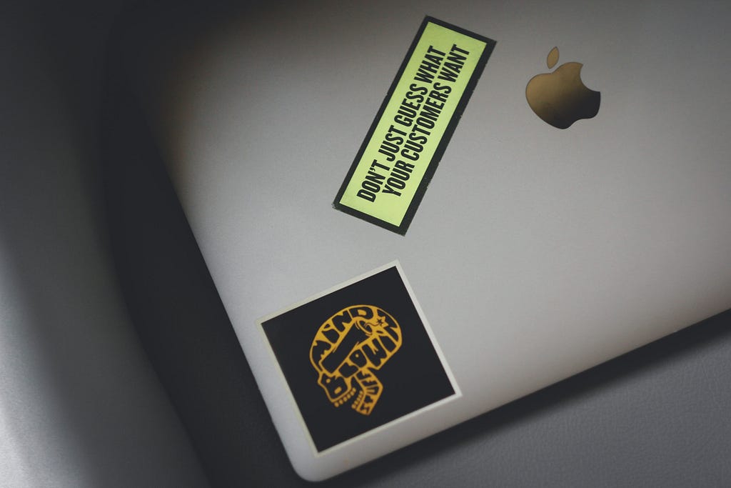 A closed Apple laptop with a sticker of a skull and another sticker that reads: Don’t just guess what your customers want.
