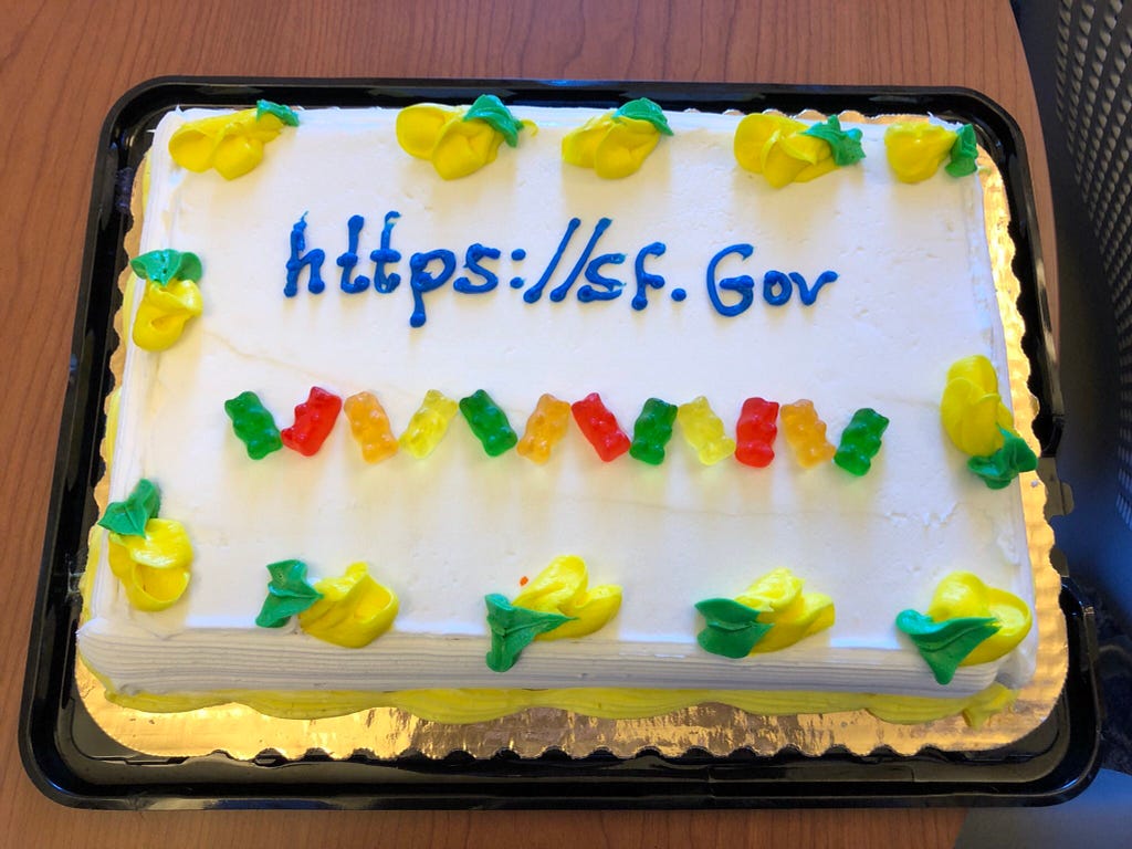 A white sheet cake decorated with yellow and green frosting and gummy bears. In slightly wobbly blue writing in frosting is the web address https://sf.gov