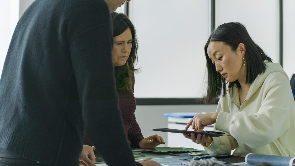 Medium shot of a color designer showing another designer color samples. They are leaning over a table full of greens and blues.