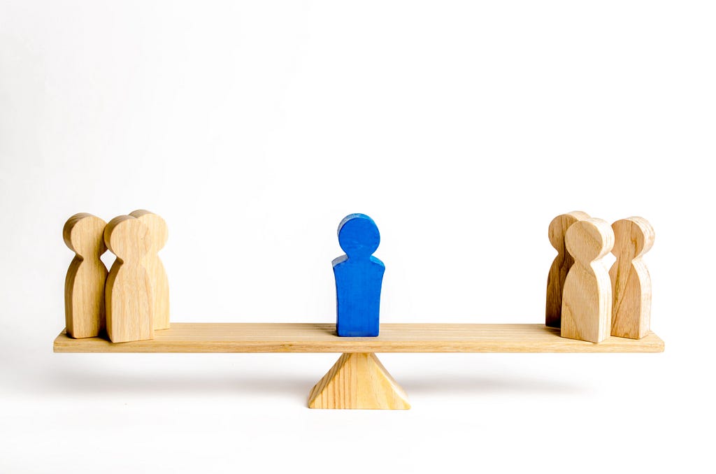 A balance with groups of wooden figures on opposite ends of the scale evenly balanced.