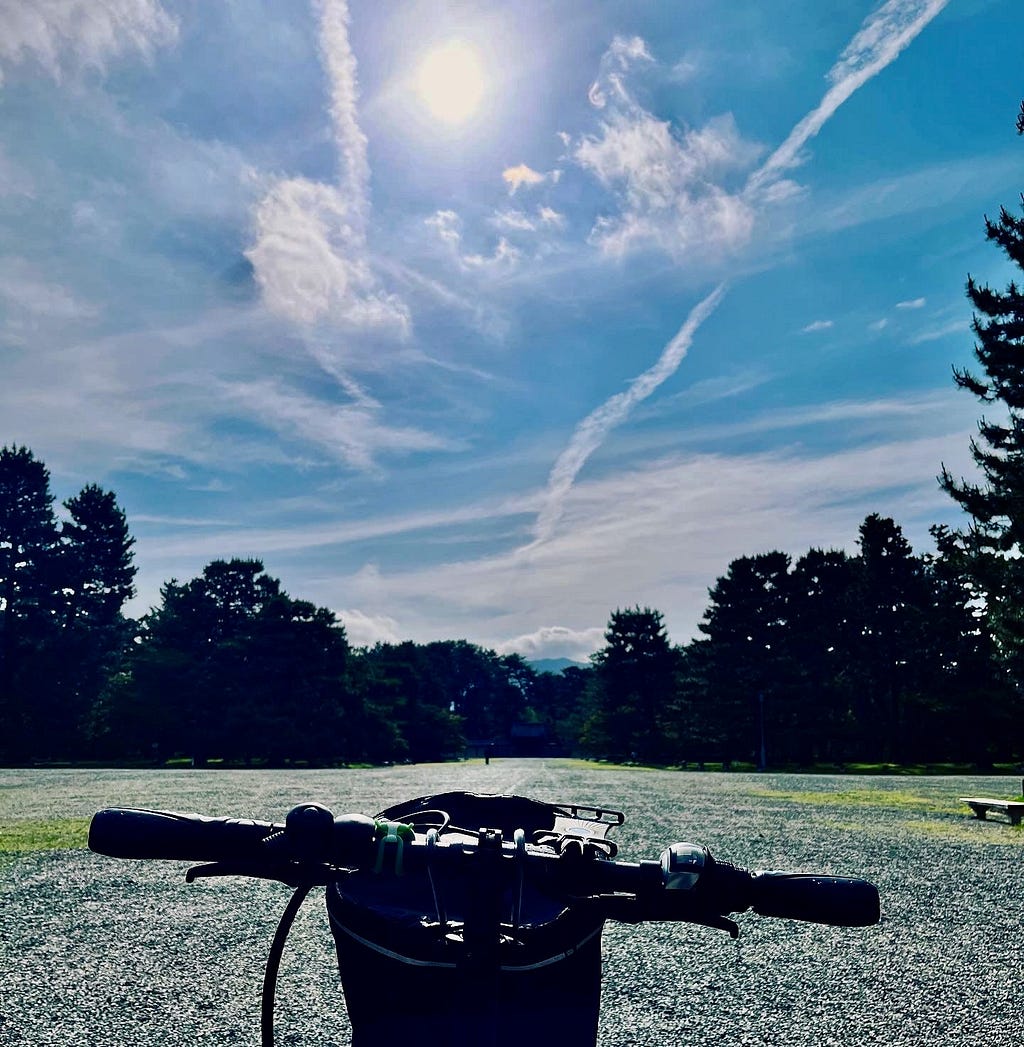 A big blue sky with wispy clouds and a bicycle view of a wide open space at Kyoto Imperial Palace Park