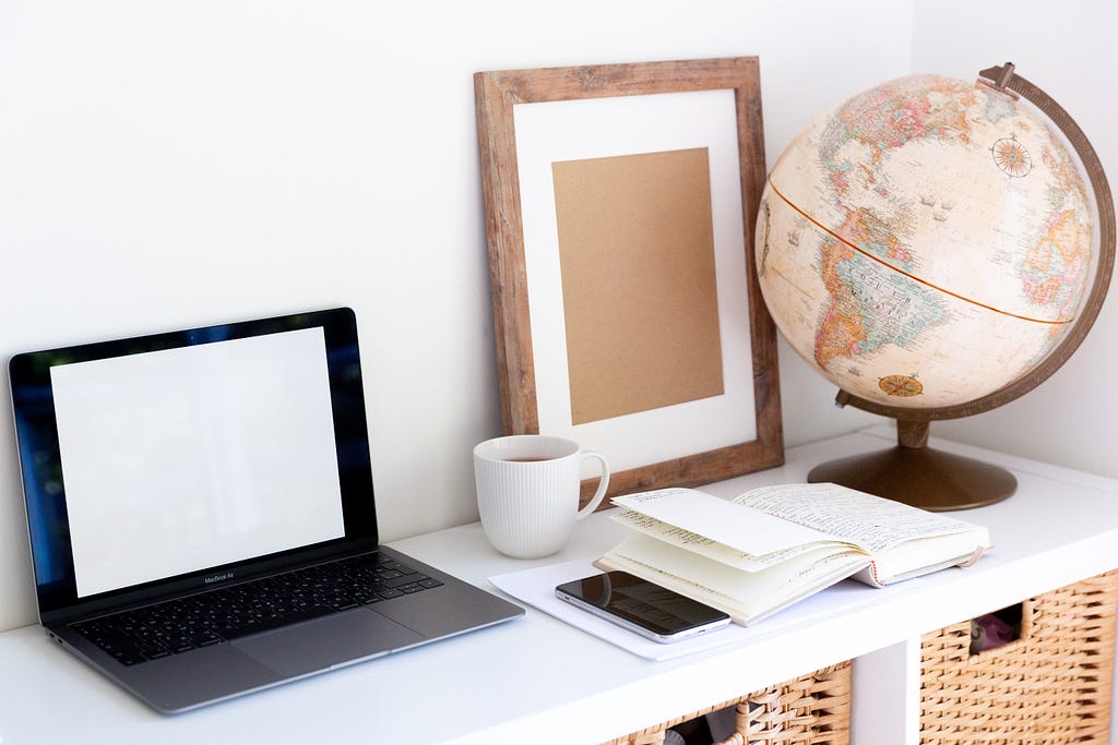 Creative workspace with vintage globe near empty frame planner and modern gadgets