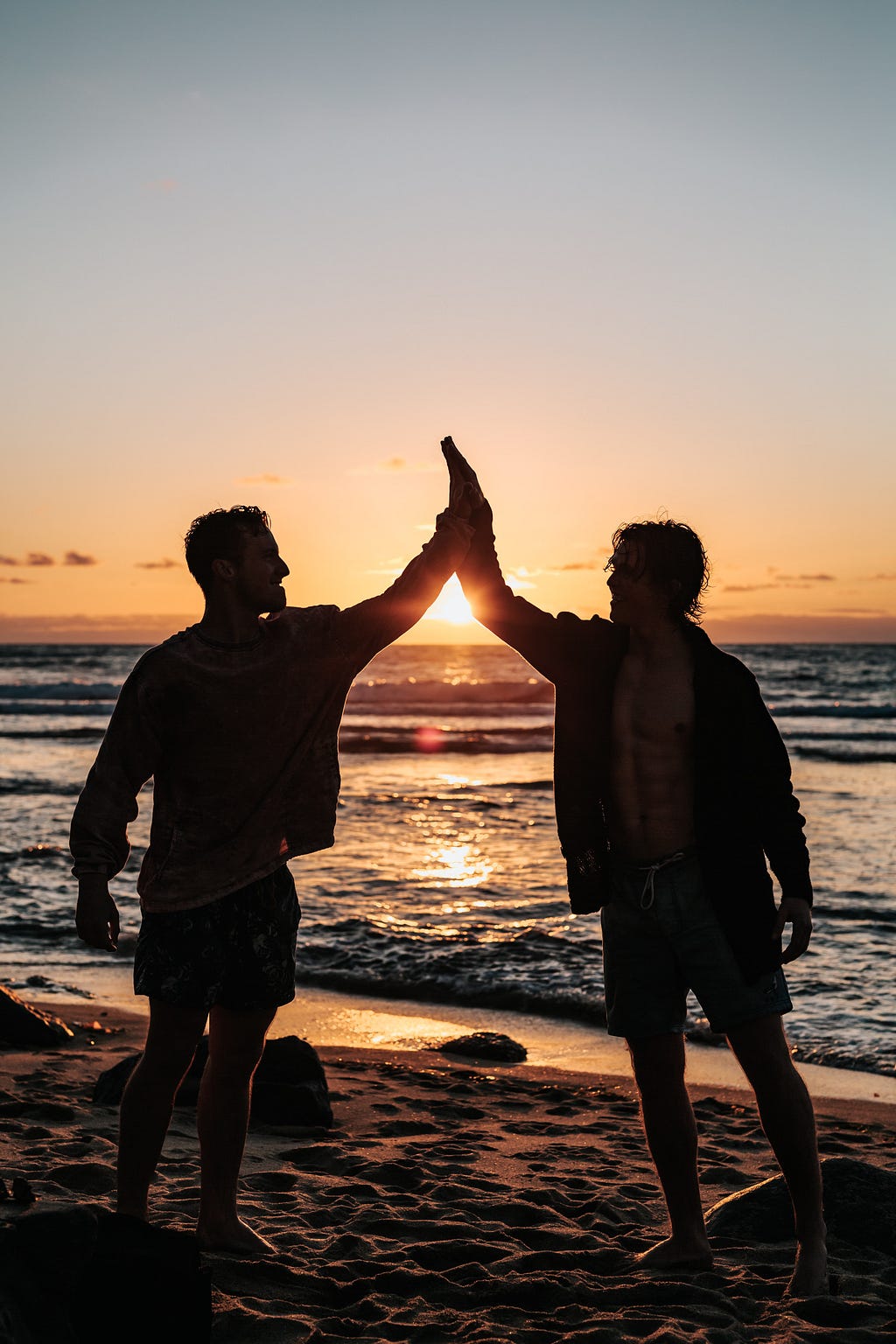 Two young men high five each other in front of a beautiful beach sunset