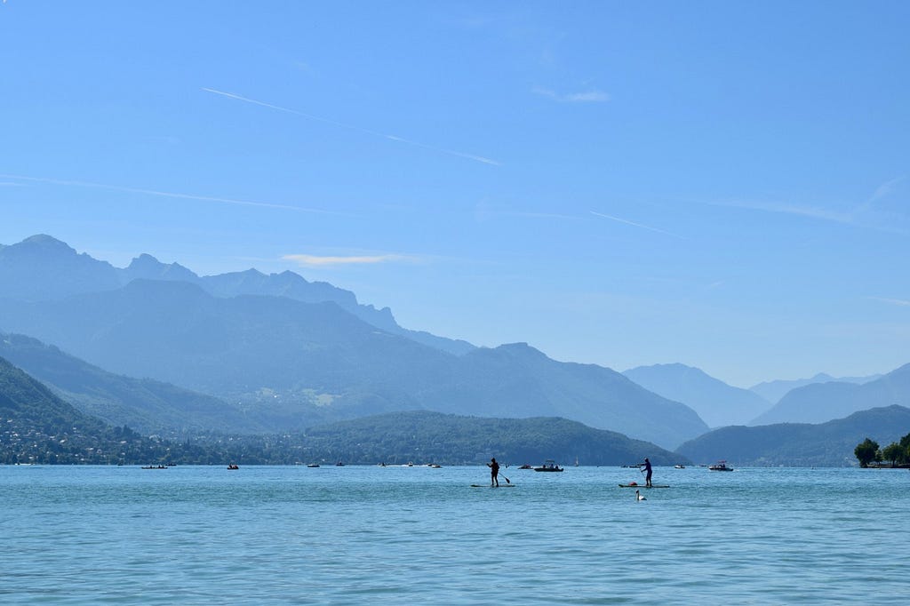 Two people paddle past a swan during an afternoon on Lake Annecy.