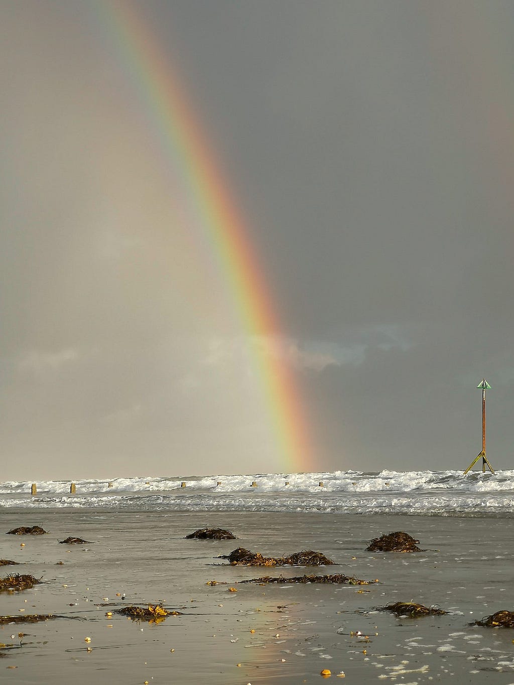 Dark skies out at sea and rainbow, waves and sand in foreground