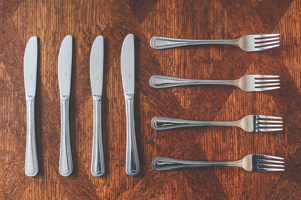 Photo of an arrangement of 4 knives vertically oriented on the left and 4 forks horizontally oriented on the right