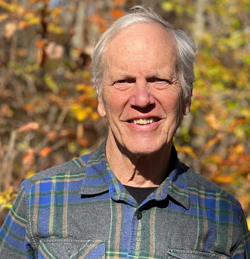 Photo of Dan Fisher smiling outside in front of Fall leaves.