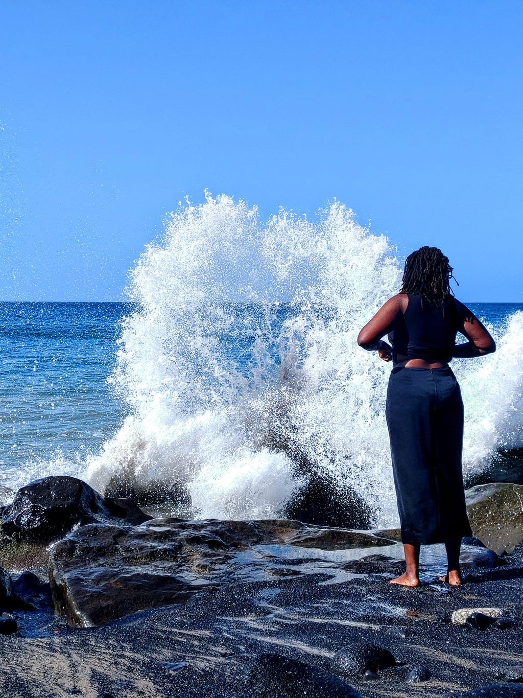 A Caspar David Friedrich-esque young me, donning all black garments, standing before a crashing wave on a rocky beach