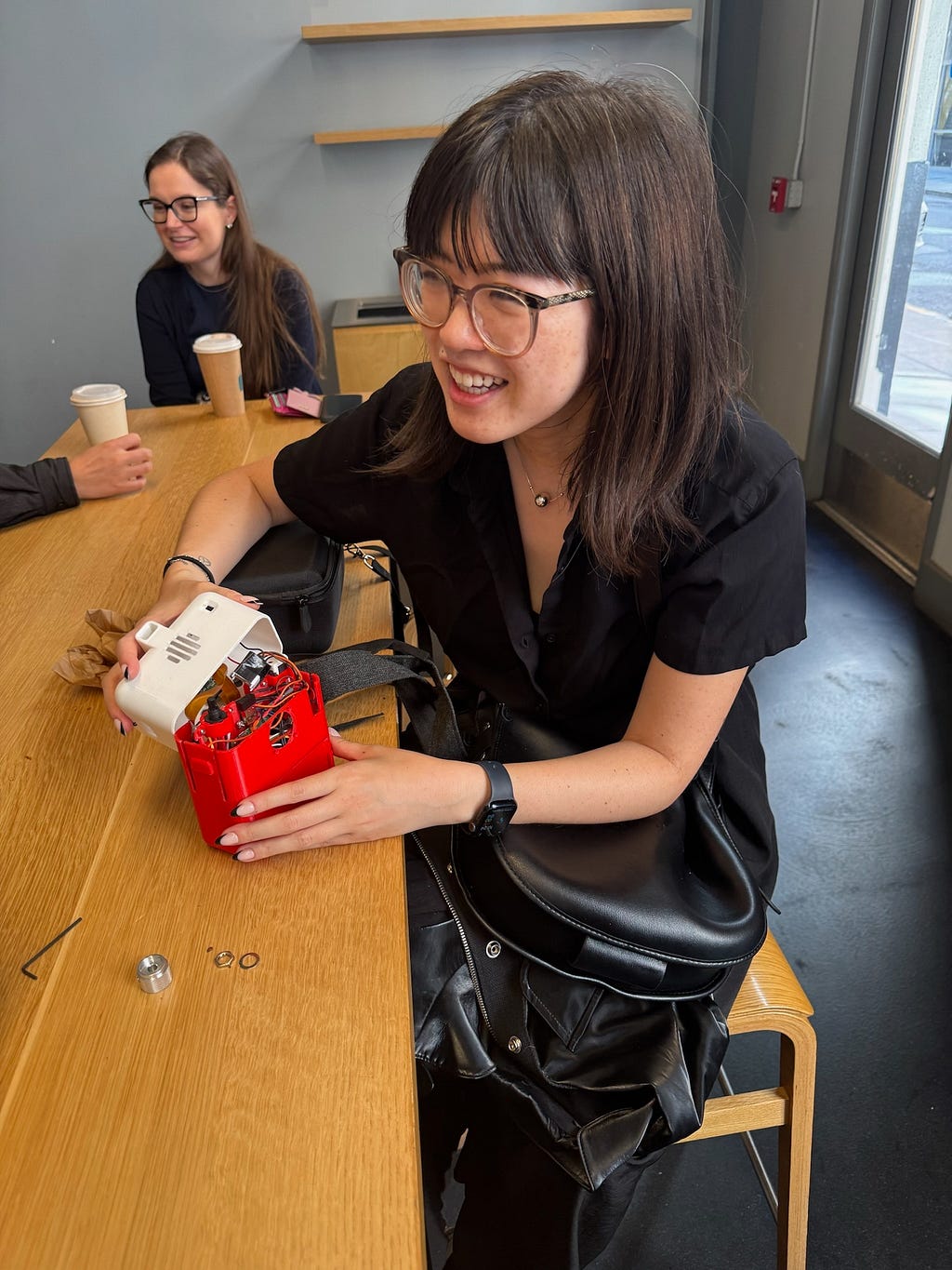 Kelin sitting at a desk holding the components of Poetry Camera and smiling.