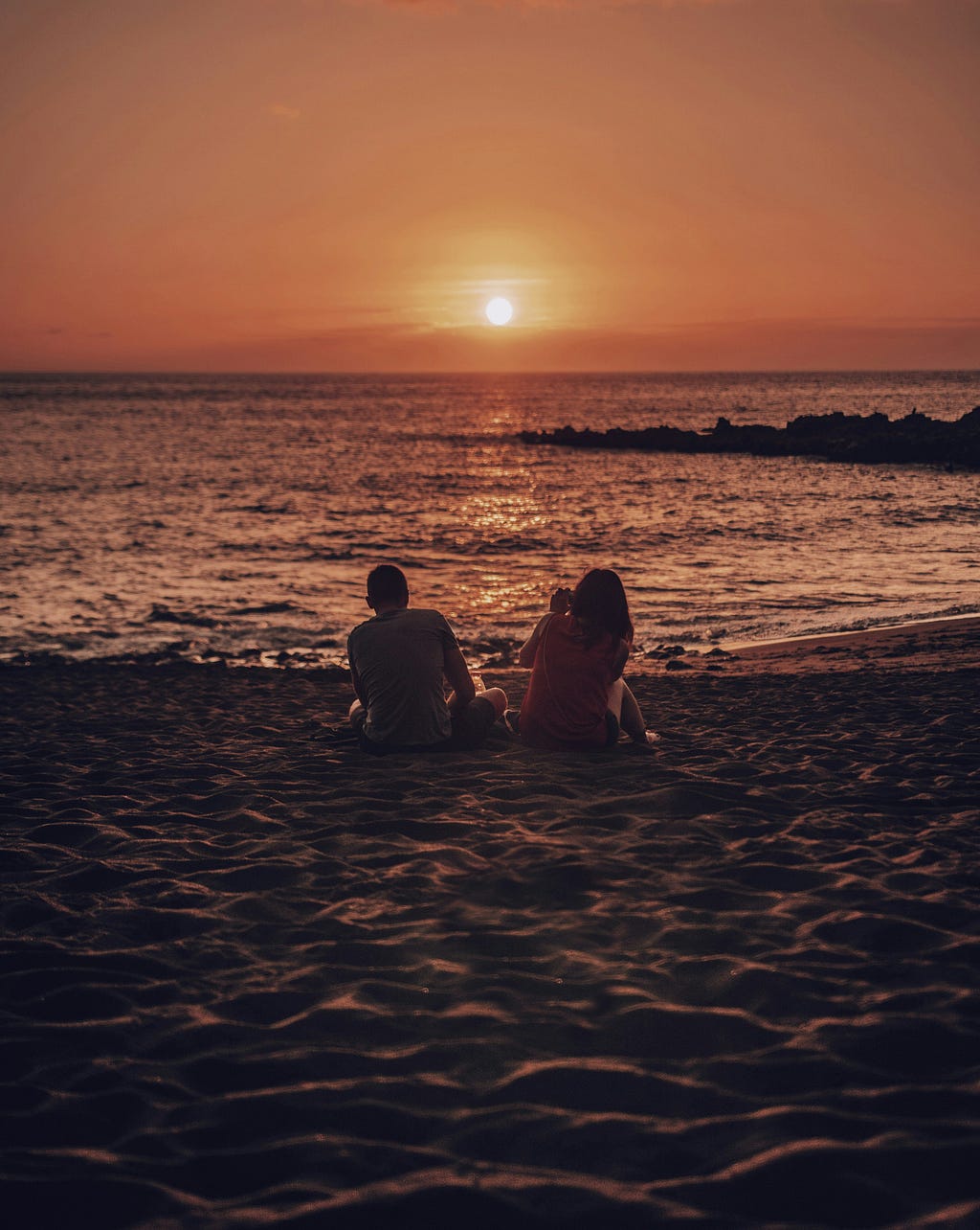 silhouette of a sitting couple looking out into the sunsetting over the calm ocean