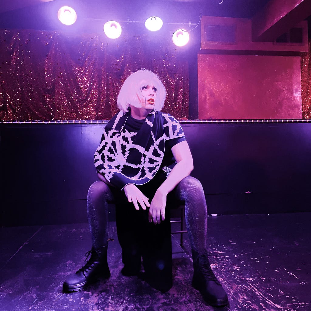 A photo of me on a small stage wearing a skirt and a shawl and a wig and makeup to make me look like an android woman