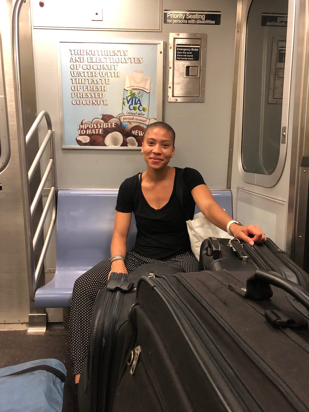 A smiling woman sitting on a NYC train surrounded by suitcases.