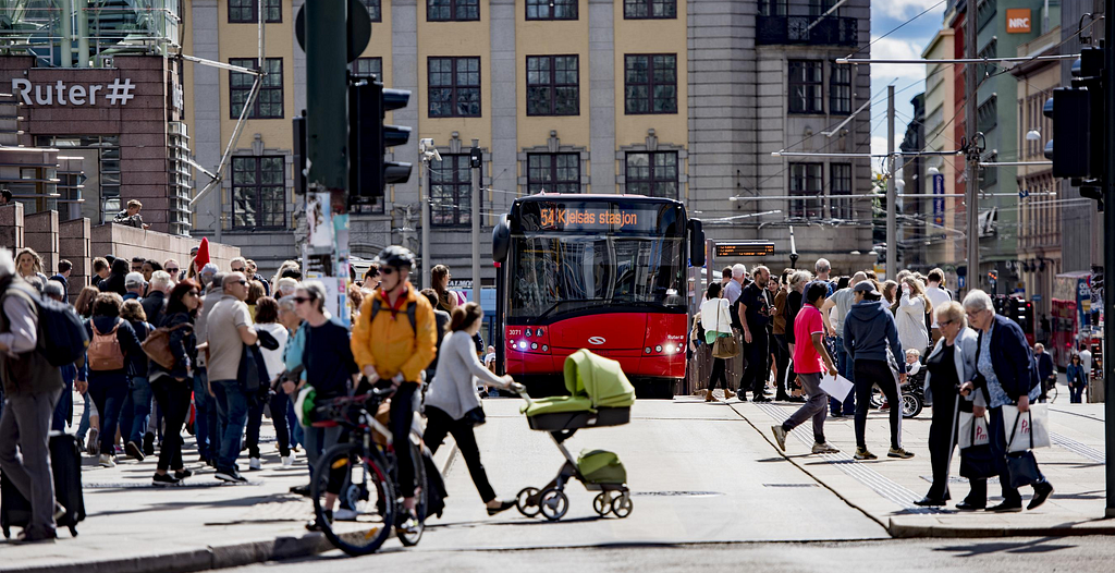 En vårdag midt på Jernbanetorget, med masse mennesker overalt, og en buss som står på en av holdeplassene.