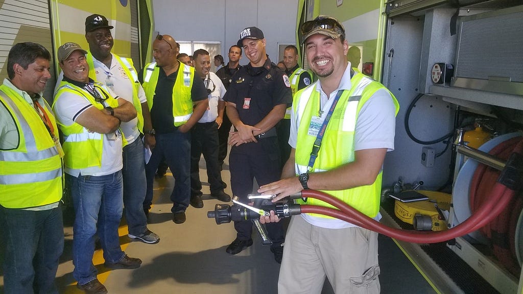 Alex in the Airport Workshop holding a hose with coworkers.