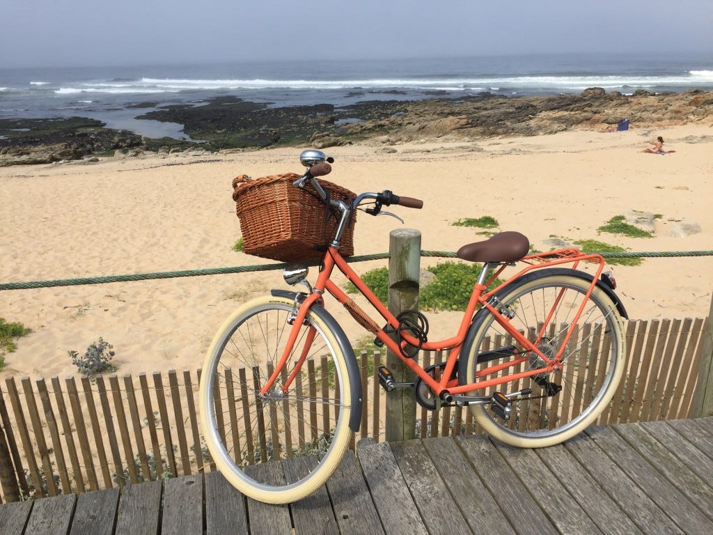 Orange bike with basket leaning against a post beside the beach