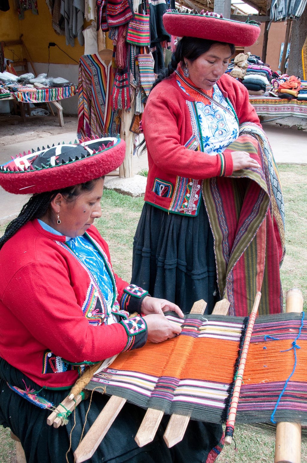 One woman from the village of Chinchero works on a backstrap loom while another folds a shawl in Chinchero, Peru. (© April Orcutt. All Rights Reserved)