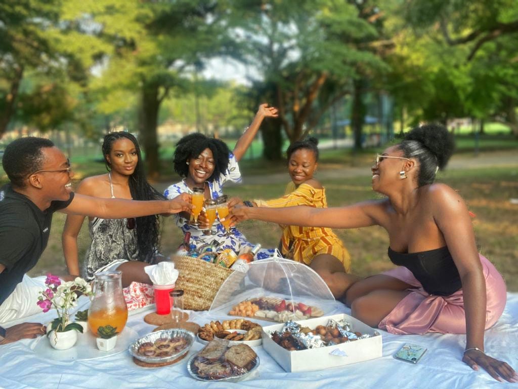 5 friends seated around a picnic, taking a toast with mimosas and smiles