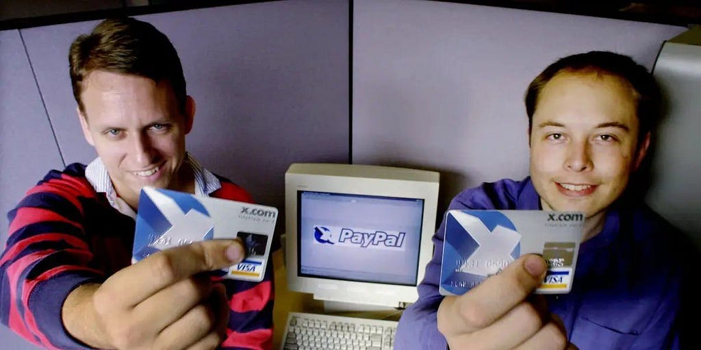 PayPal icon on Monitor and x.com card in hands of Elon Musk and Peter Thiel