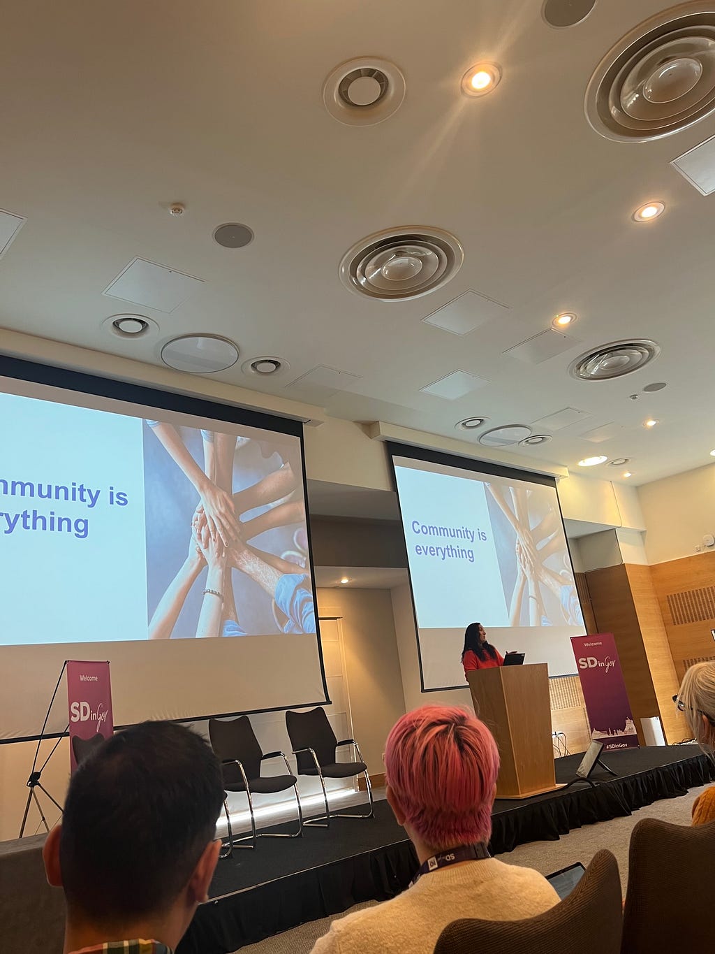 Rochelle Gold stands at a podium, in front of slide that says “community is everything”