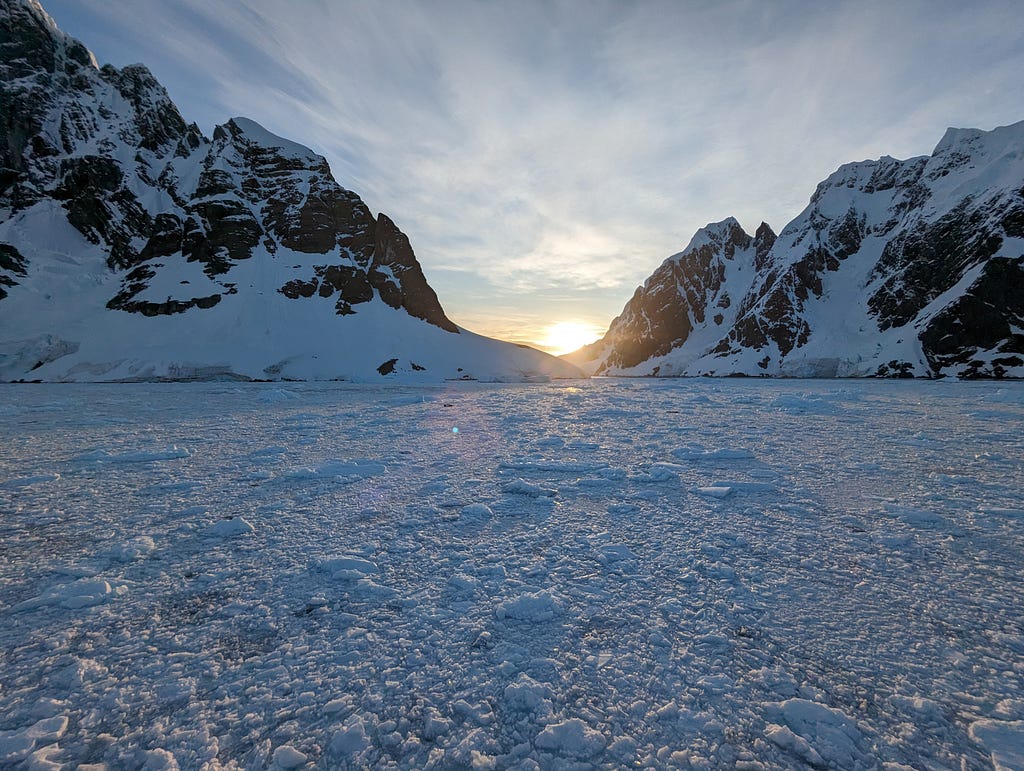 The sun setting on Antarctica behind the mountains rising from a sea of ice