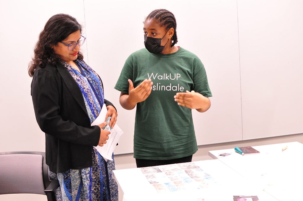 Cambridge Mayor Sumbul Siddiqui looks at a t-shirt on a table while a student from Cambridge Rindge and Latin School talks about it.