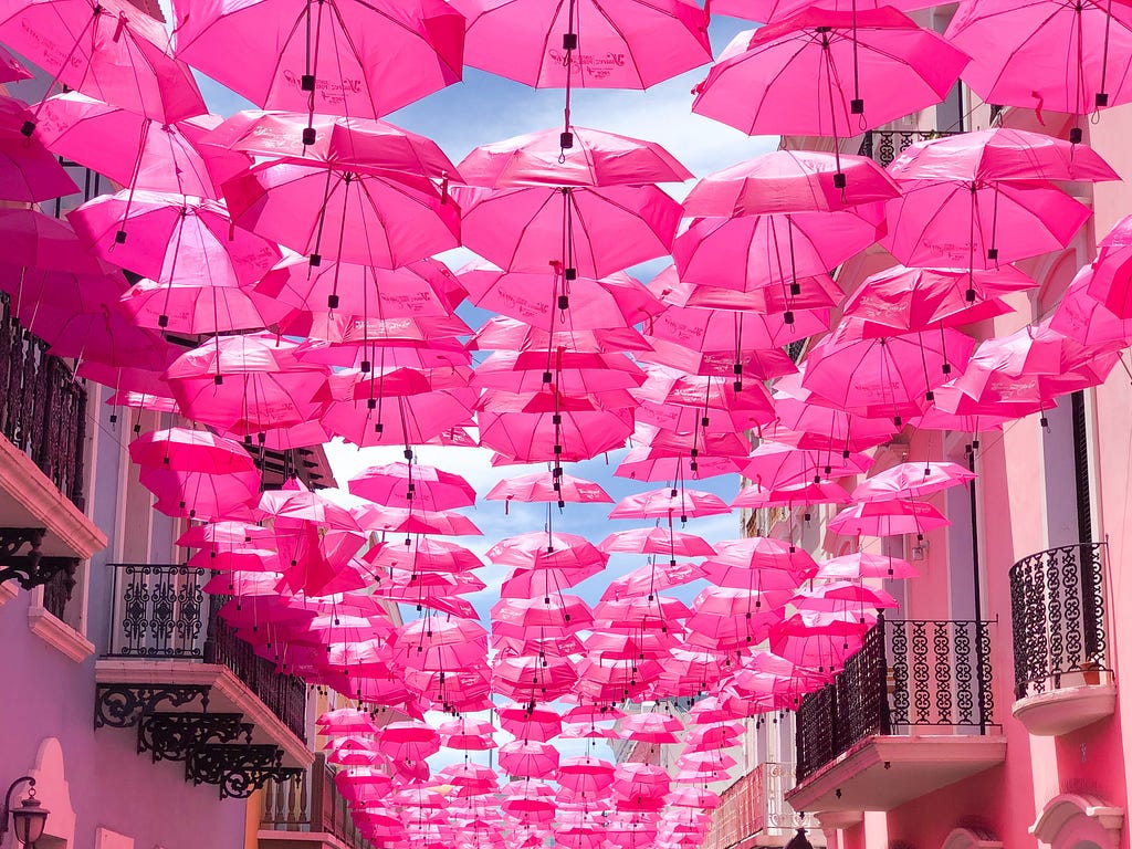pink umbrellas hanging between two pink buildings