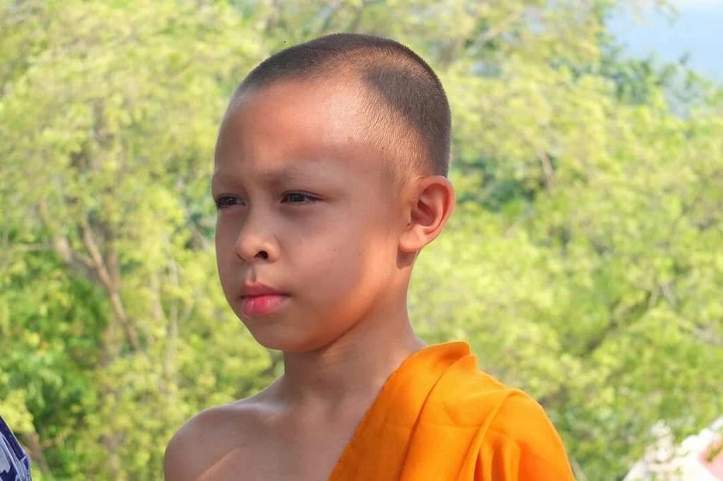 A young boy in Thailand in the traditional orange garb of a Buddhist monk.