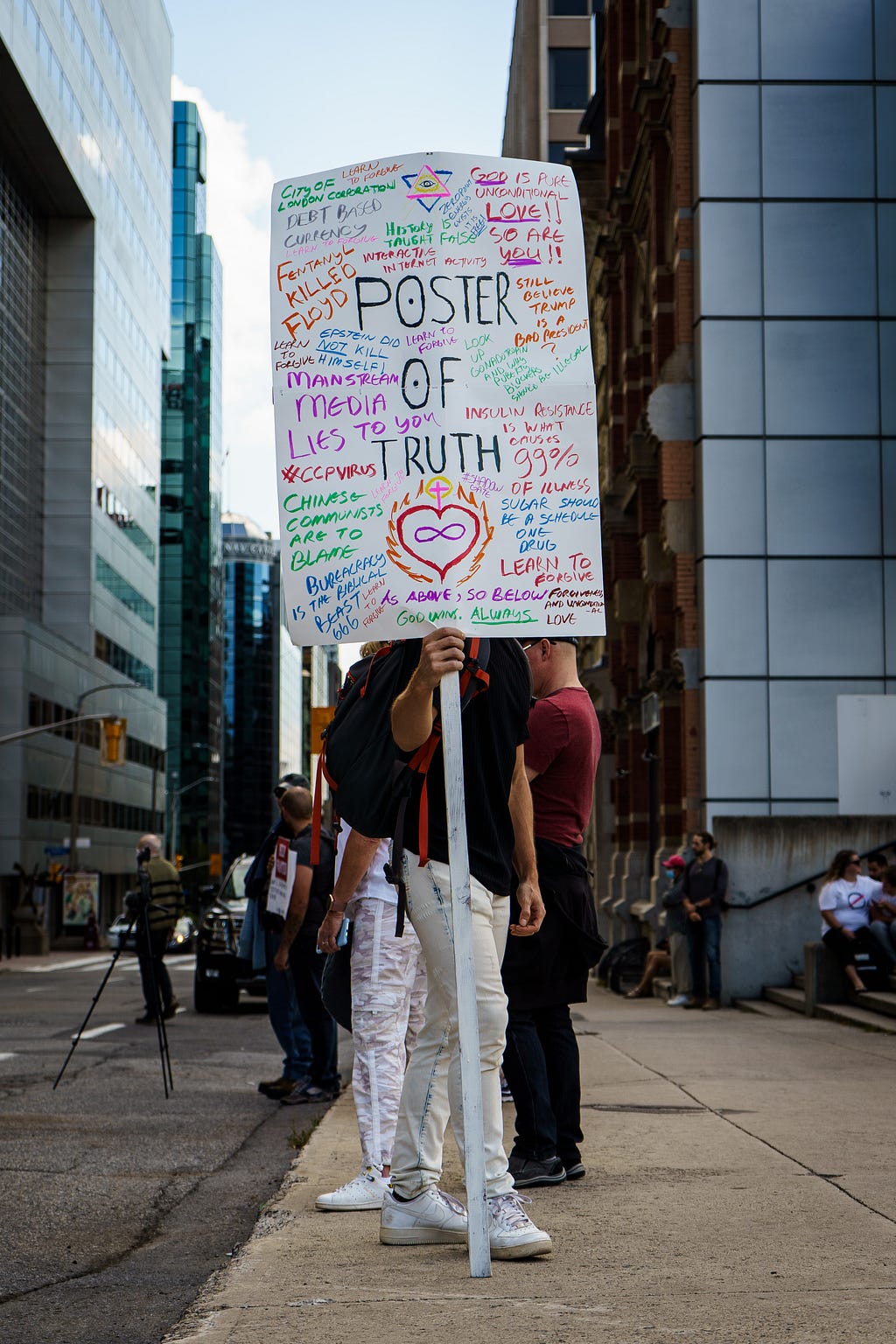 Person holds up a placard with a variety of conspiracy theories written on it