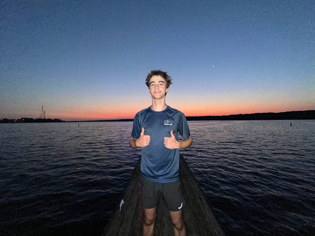 Photo of a teenager standing in front of a body of water with two thumbs up.