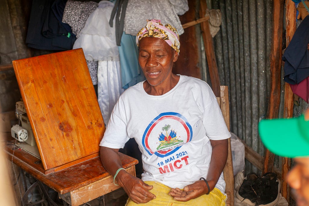 Elinise Joseph talks with door-to-door distributors in her home as she takes a break from her sewing business to receive a dose of LF medicine. Photo credit: RTI International/ Emmanuel Riscka Chery