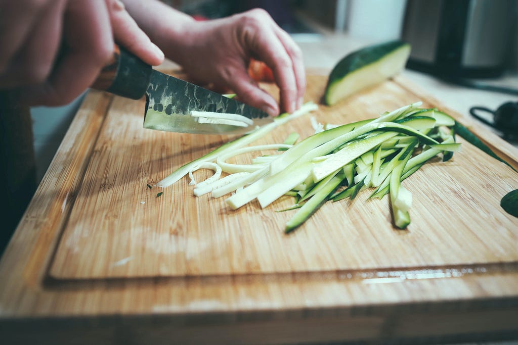 Hands cutting cucumber on a cutting board.