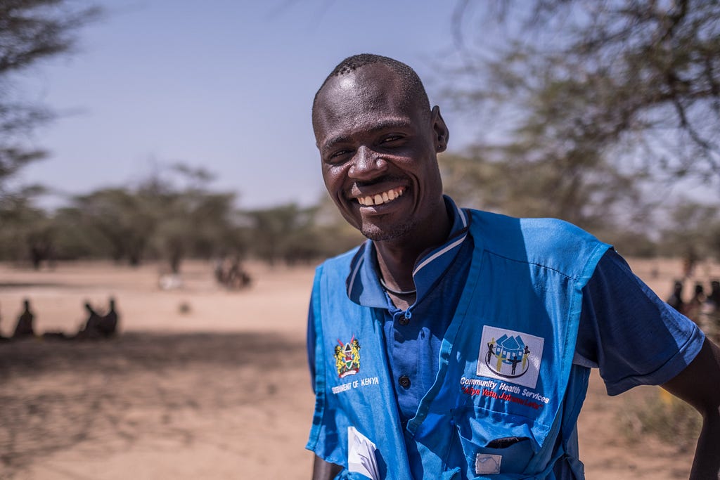A portrait of community health volunteer James Lomuria standing in the barren Turkana landscape