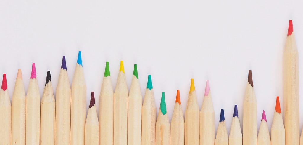 Photo by Jess Bailey on Unsplash showing a line of brightly colored pencils lined up at different heights
