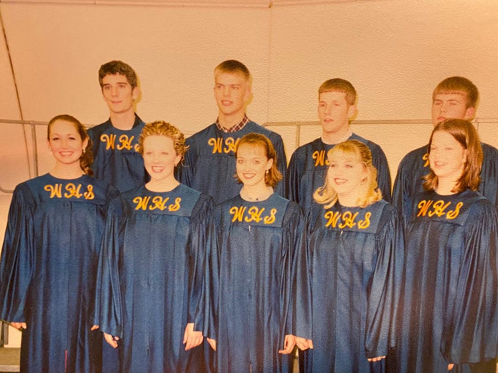 Nine high school students dressed in blue choir robes that have the letters WHS embroidered on them.