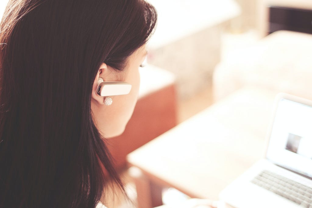 Woman at a laptop wearing a bluetooth earpiece