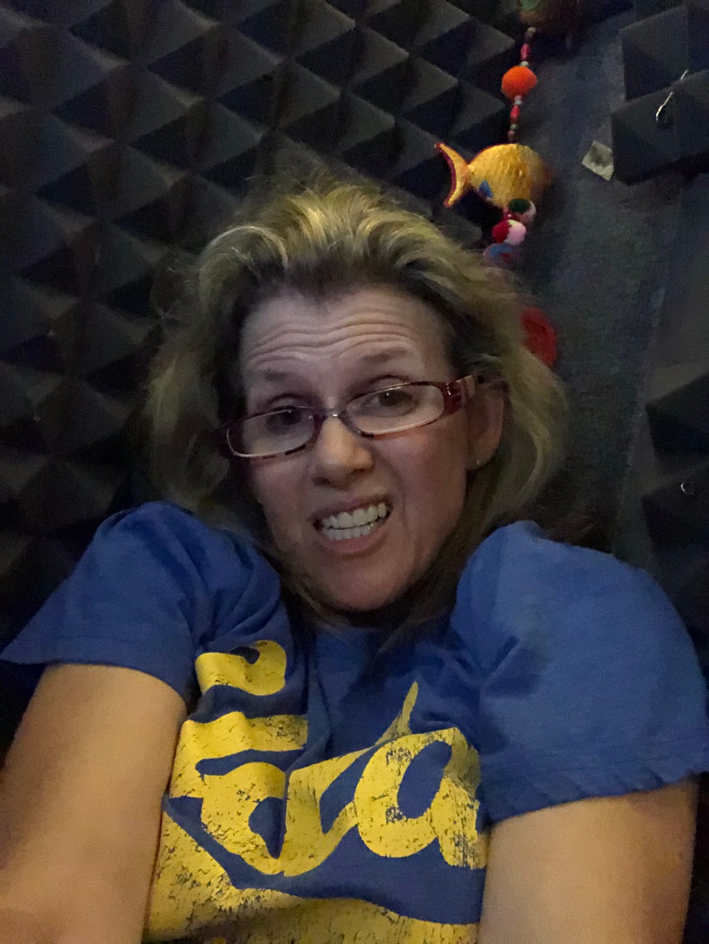 Close up of a woman’s grimacing face, in a recording booth. She is clearly very uncomfortable