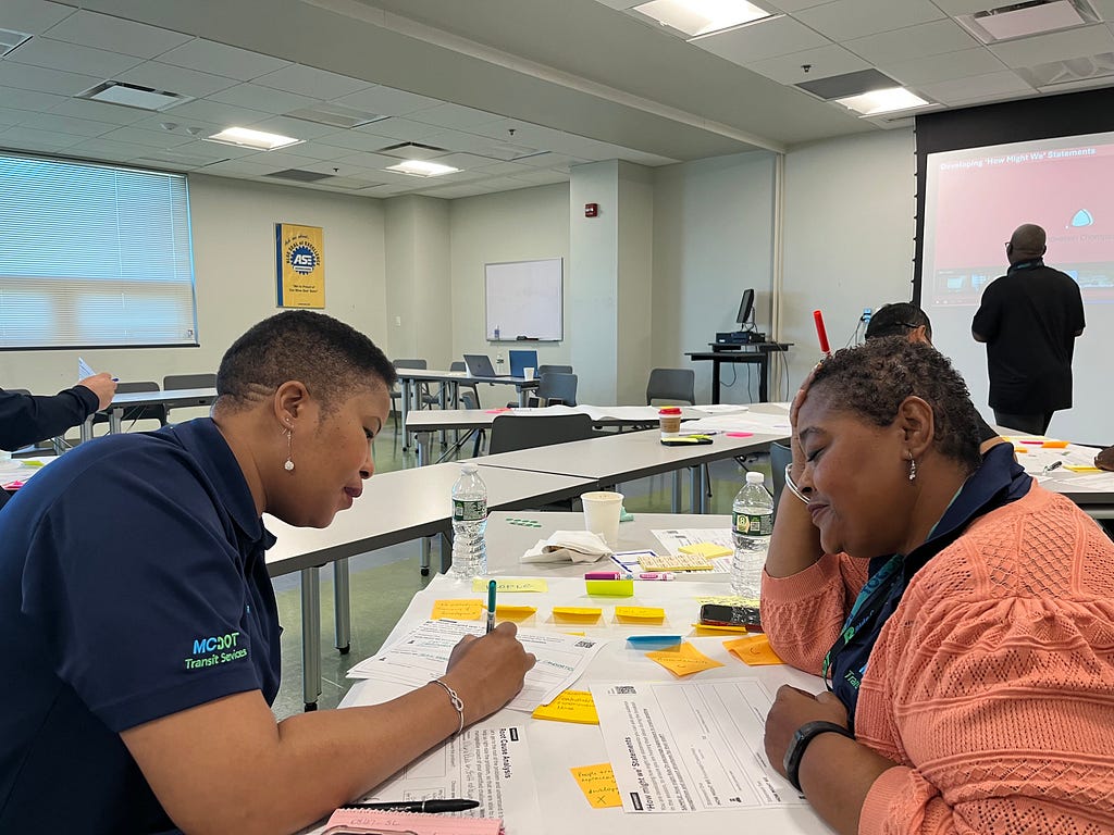 Two colleagues write on worksheets at a table together.