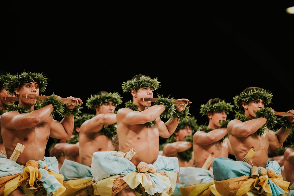 Men dancing a hula using the Hawaiian musical bow and dressed in traditional clothing.