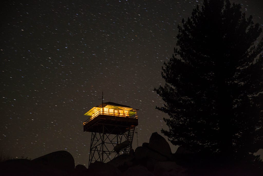 A fire lookout tower at night, with lights on inside, against a starry sky