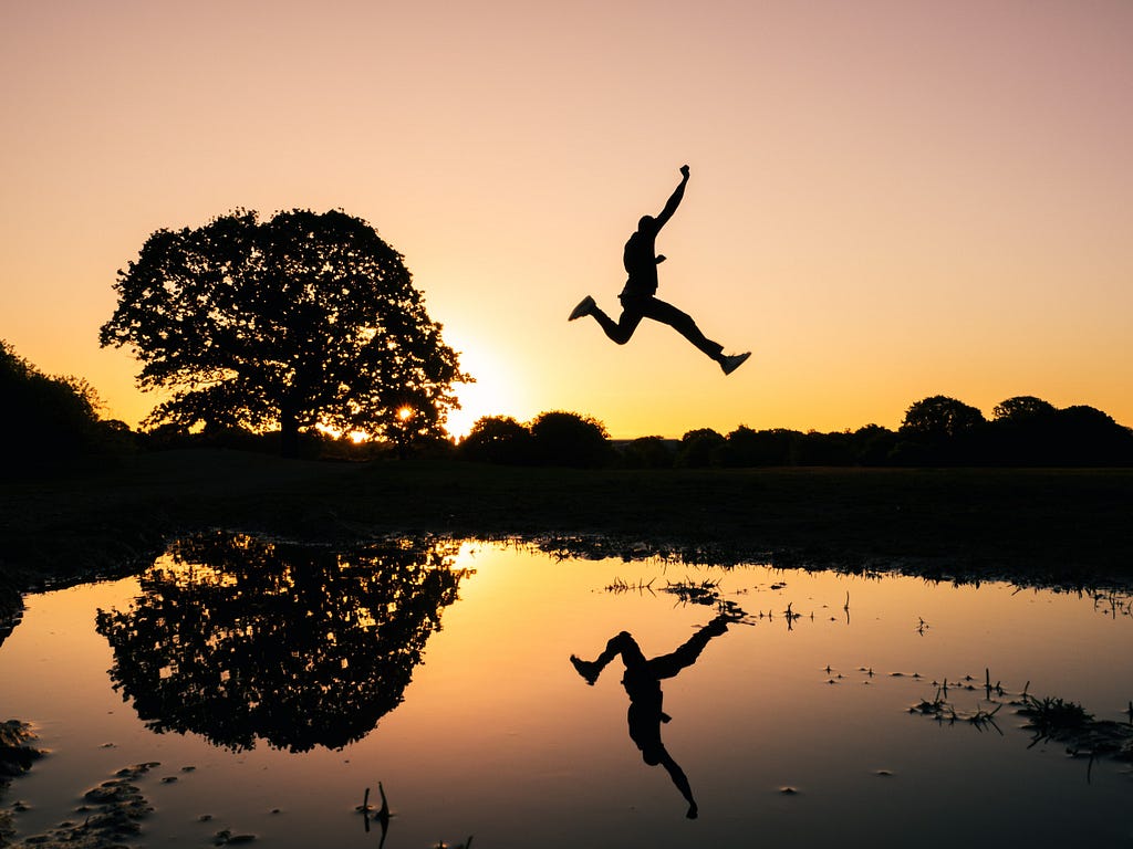 Someone leaping high above a body of water, at sunset. Photo by @kidcircus on Unsplash