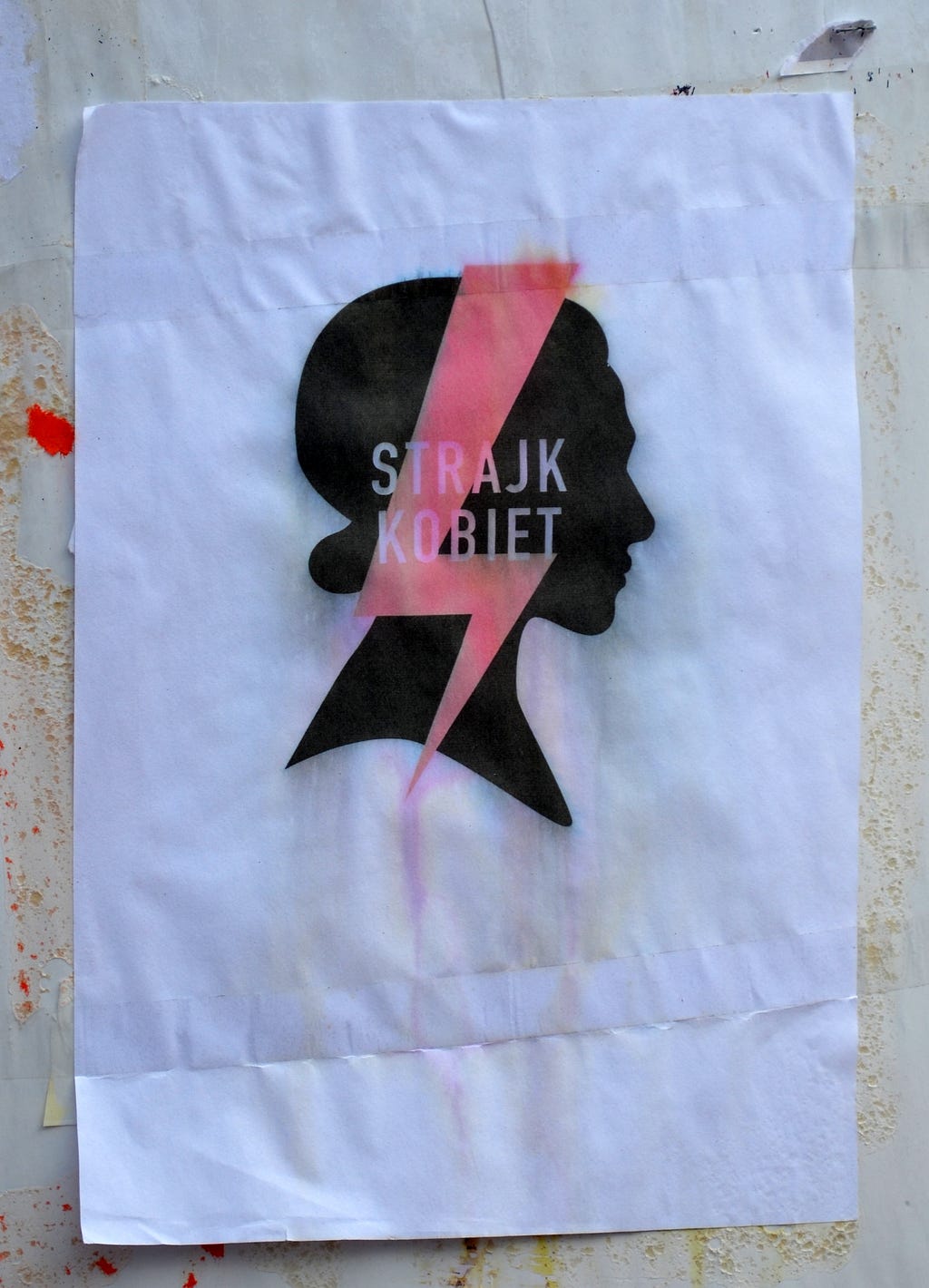 A flyer hangs on a wall in Sanok, Poland, October 2020. On a white background, a woman’s silhouette with a bright lightning bolt and the words, STRAJK KOBIET / WOMEN’S STRIKE