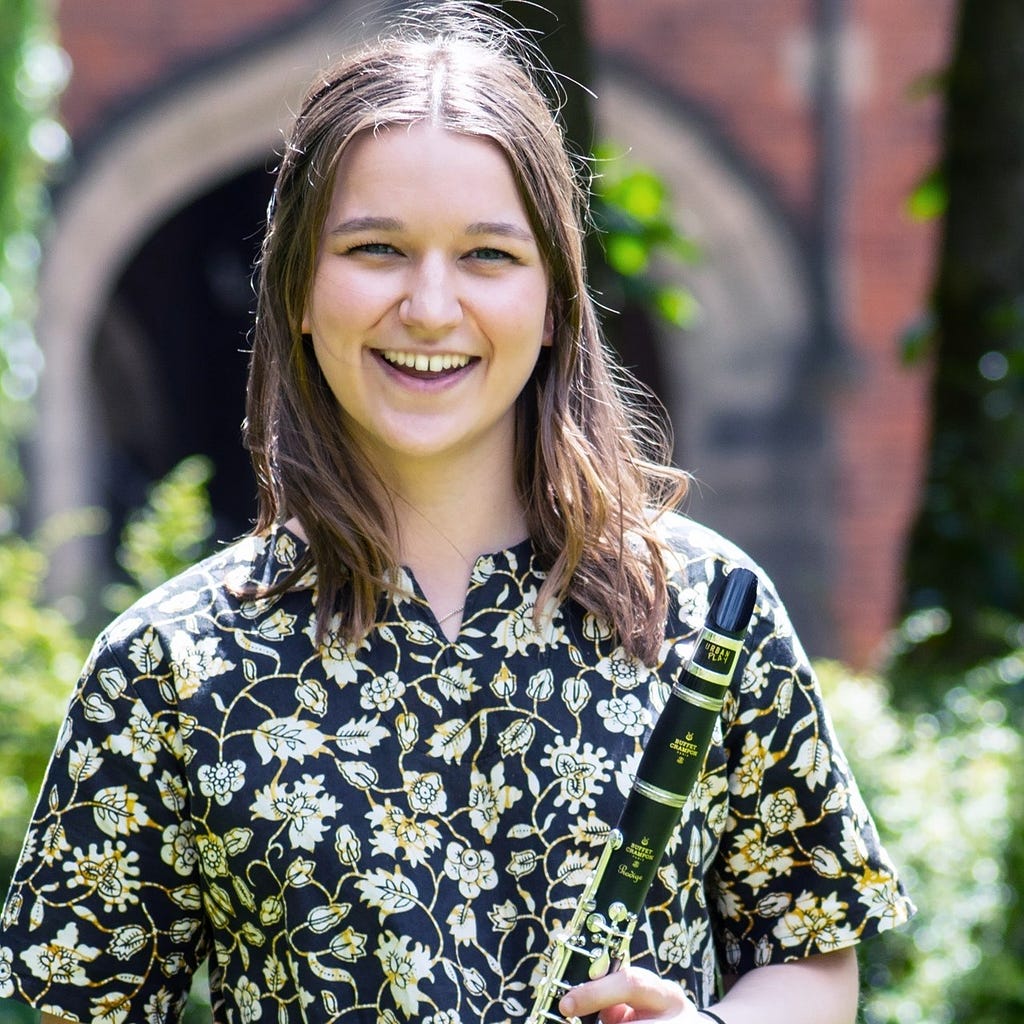 A headshot of Eleanor, Volunteering Engagement Assistant. Eleanor is pictured outside and is holding a clarinet.