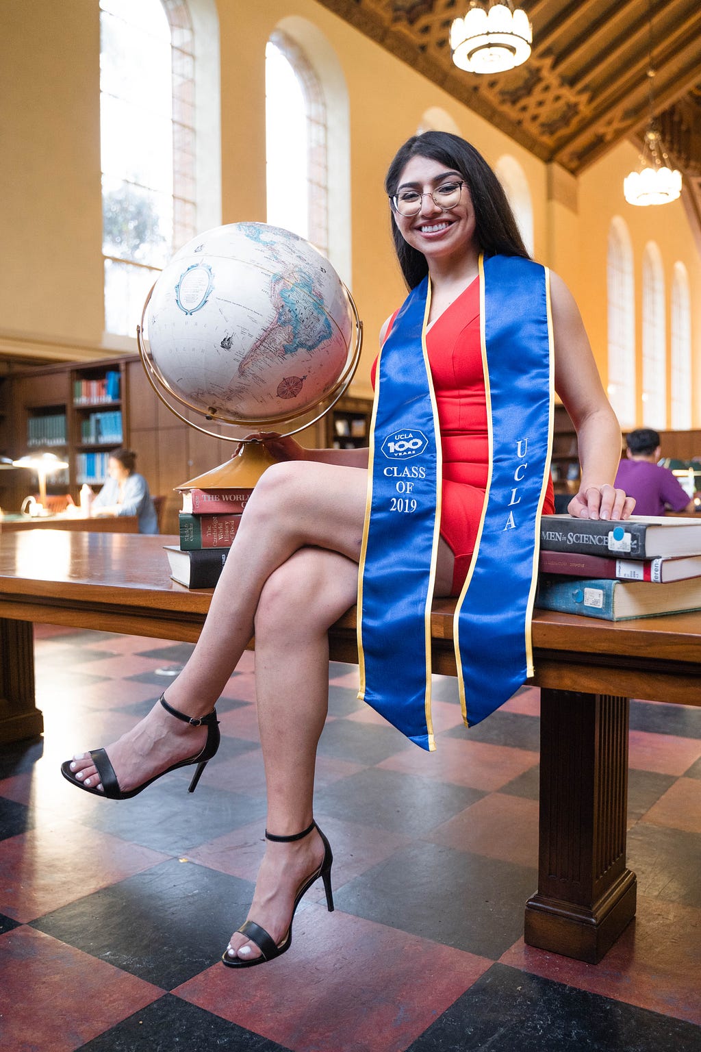 Alejandra sitting on top of a library desk with her graduation sash on