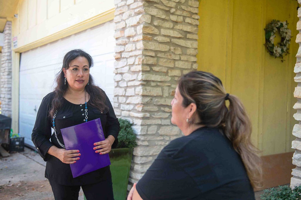 A woman interviews another woman outside her brick home in Austin.