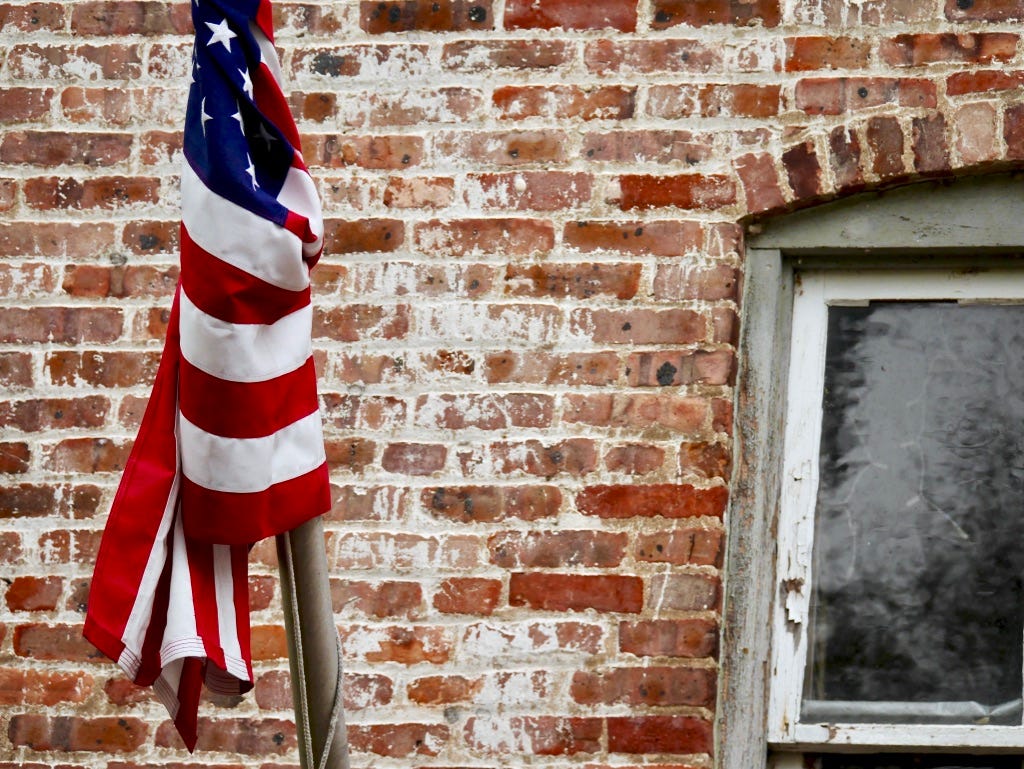 An American flag is wrapped around a flag in front of a brick wall.
