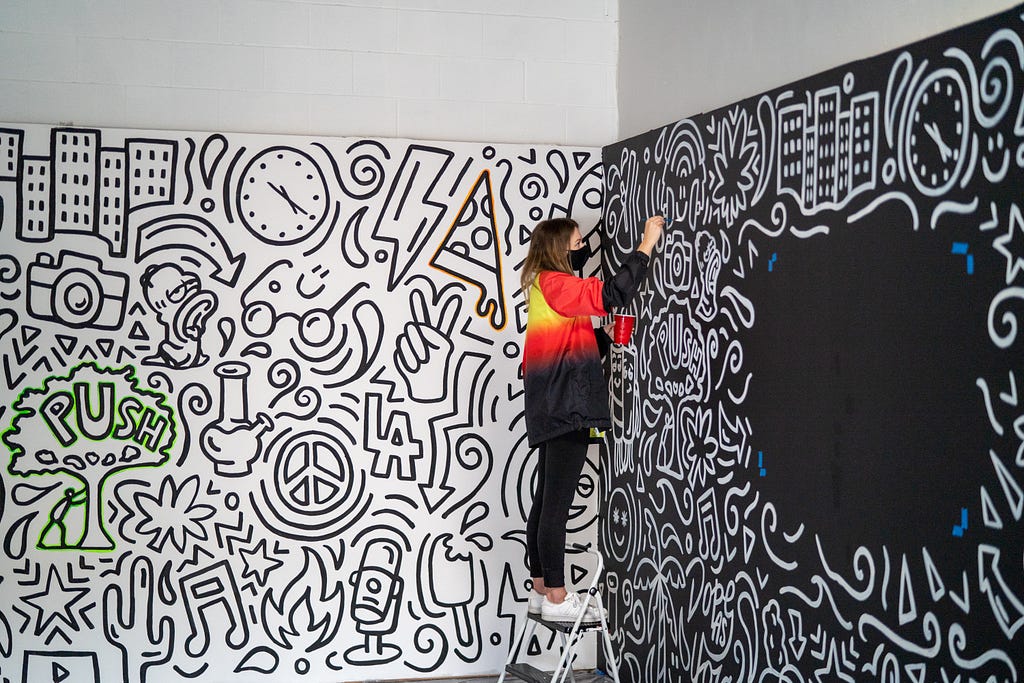 Artista em cima de uma banqueta, fazendo pintura na parede explorando contrastes entre elementos.